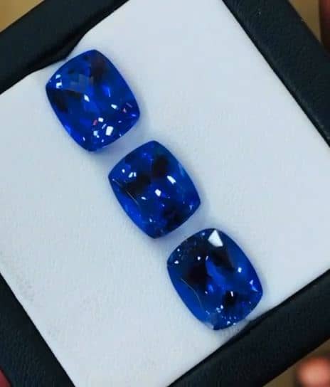 Three cushion-cut blue stones of matched size and colour, set out in a white display box.