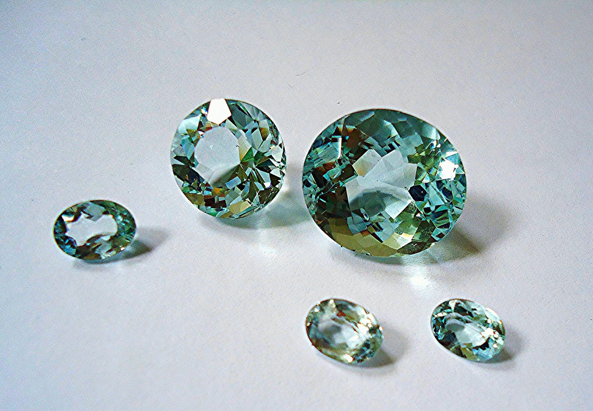 Five faceted pale blue-green stones, rounds and ovals, on a grey-blue ground.