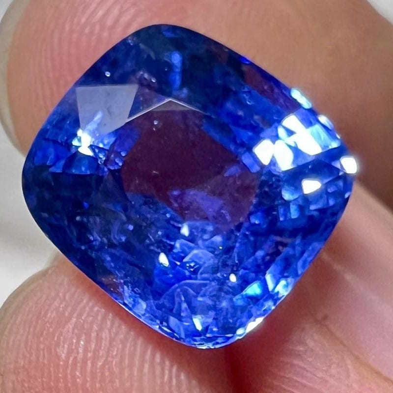 Close view of a cushion-cut blue sapphire, filling the frame, with strong blue saturation and bright facet flashes.
