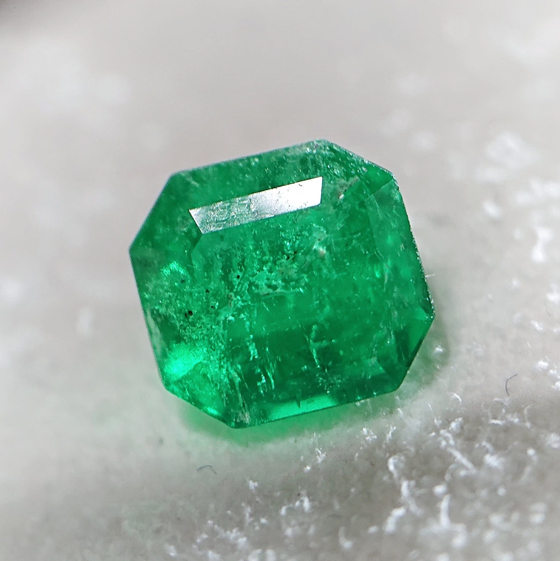 A single emerald-cut green stone resting on a white, textured surface.