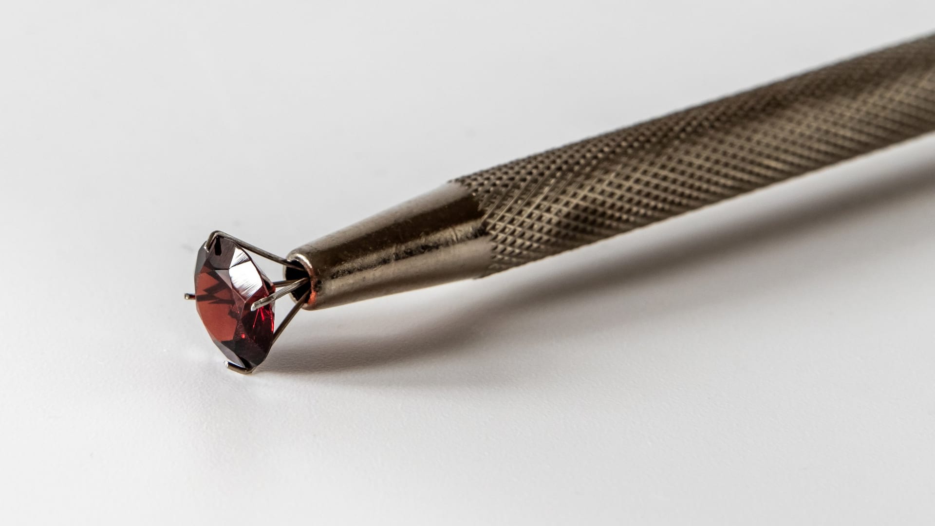 A faceted red stone held in the prongs of a metal stone holder.