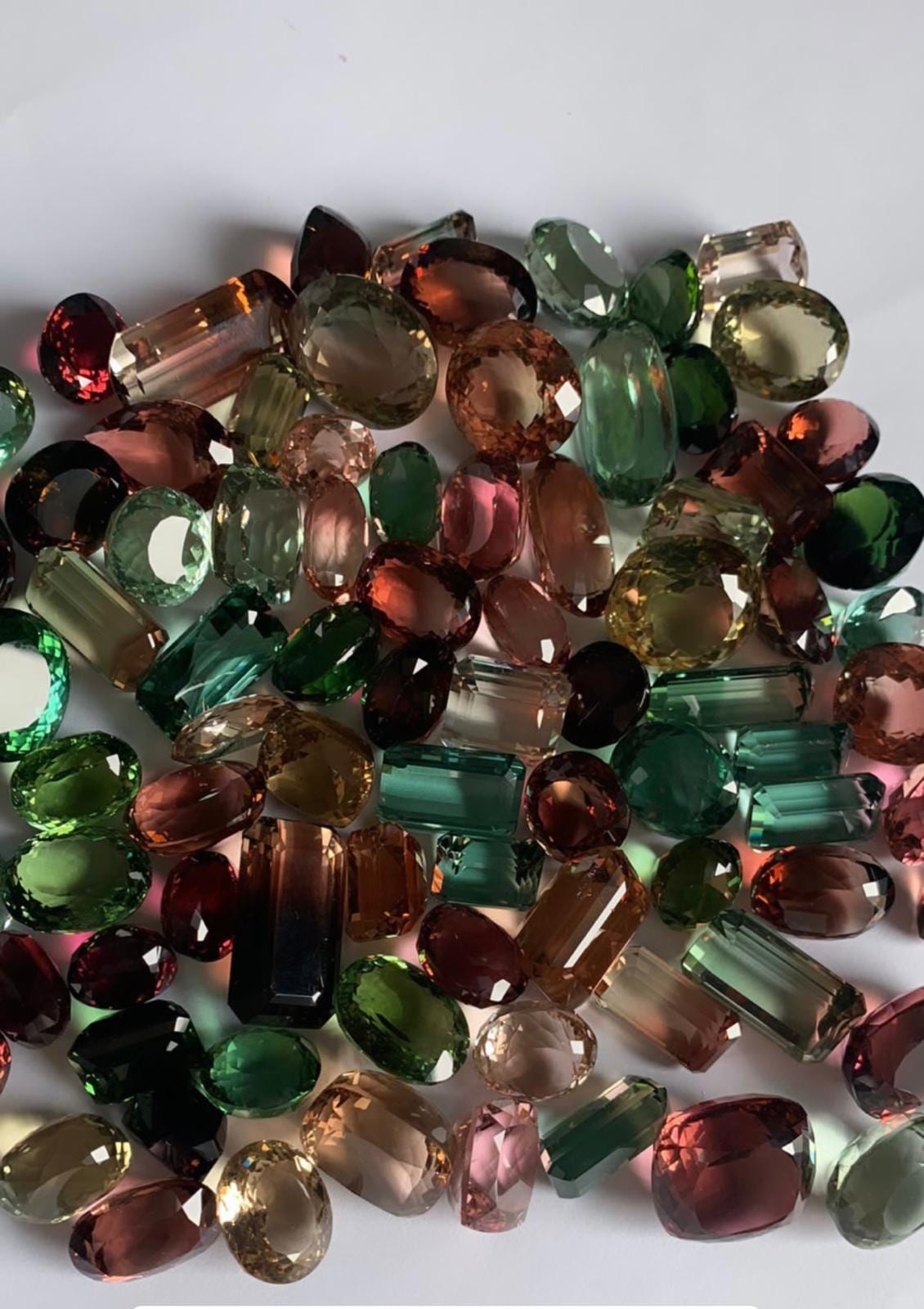 A dense parcel of faceted tourmaline in green, pink, peach, red and olive, cut as ovals, emerald cuts, rounds and pears.