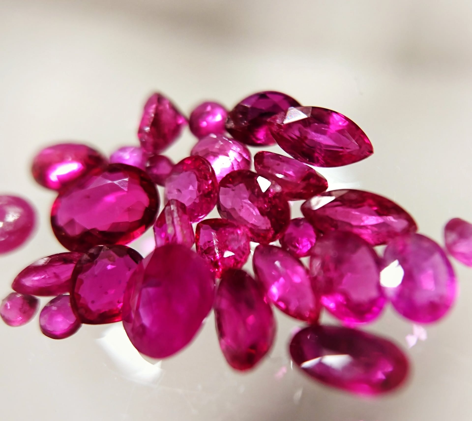 A heap of faceted red and pink stones — ovals, marquises and rounds — on a pale surface.